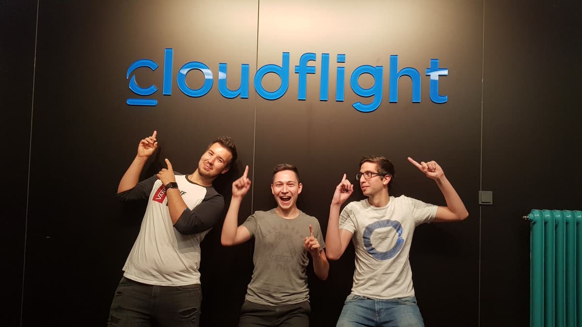 Three Cloudflight Colleagues standing next to the Cloudflight Logo