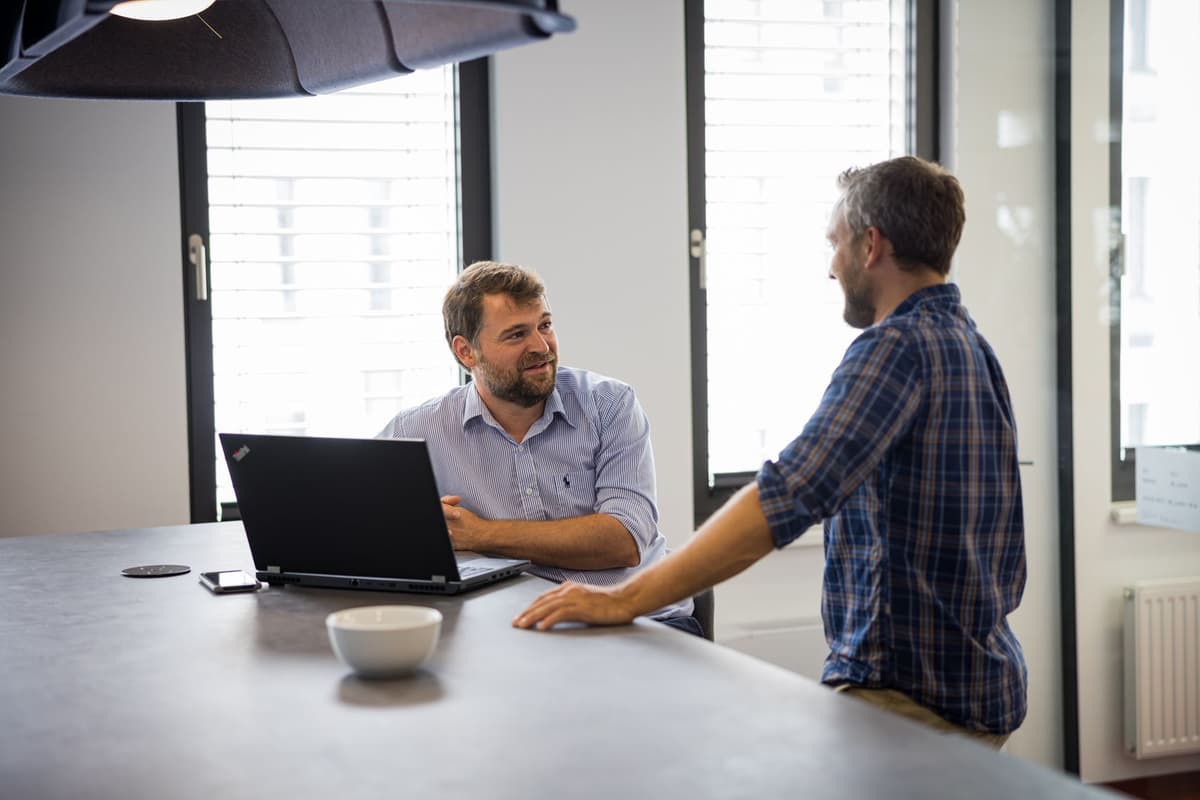 Two men discussing a project while sitting on a chair with a laptop